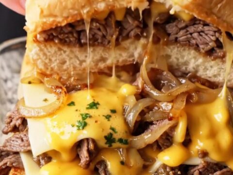 Loaded Philly cheesesteak sliders on a baking dish with golden tops and melted cheese pulling apart