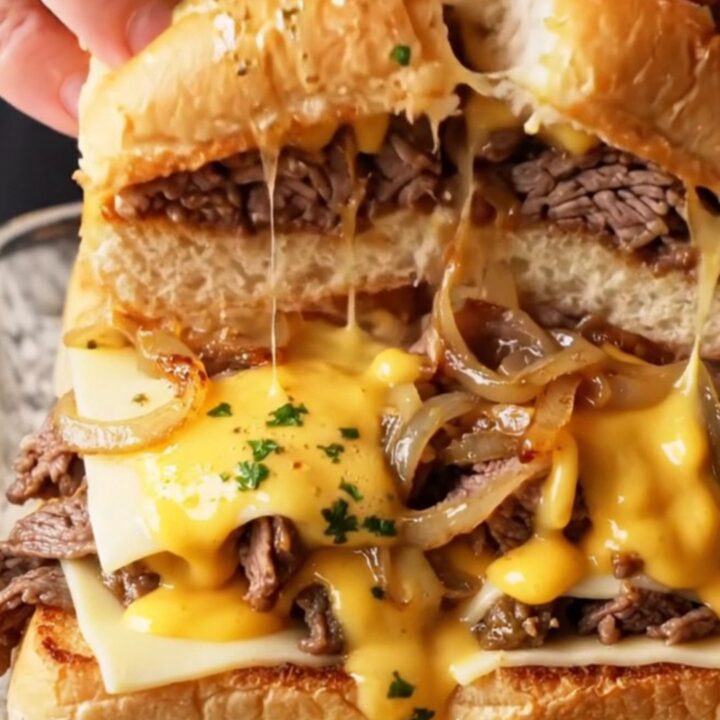 Loaded Philly cheesesteak sliders on a baking dish with golden tops and melted cheese pulling apart