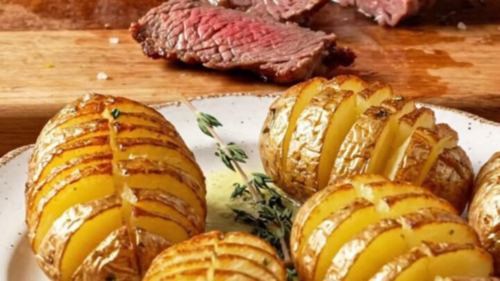 Seared filet mignon sliced and topped with garlic herb butter, beside crispy accordion potatoes