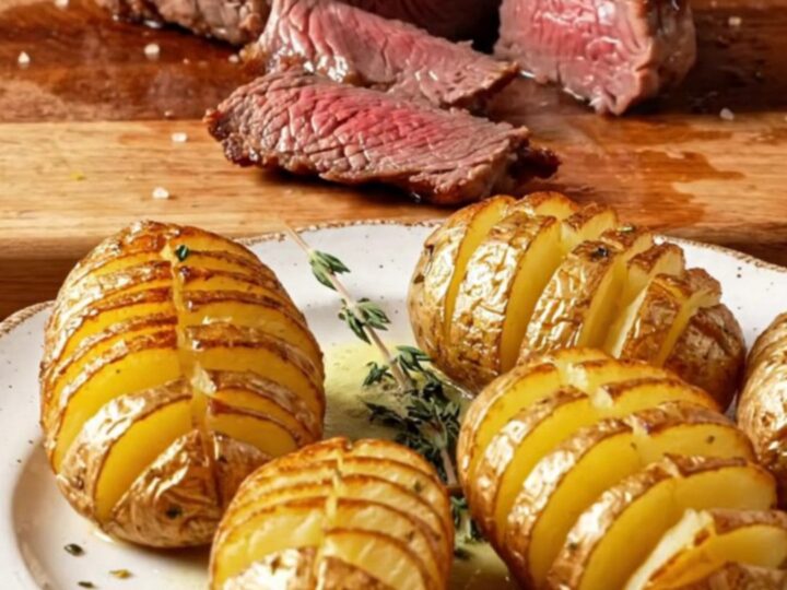 Seared filet mignon sliced and topped with garlic herb butter, beside crispy accordion potatoes
