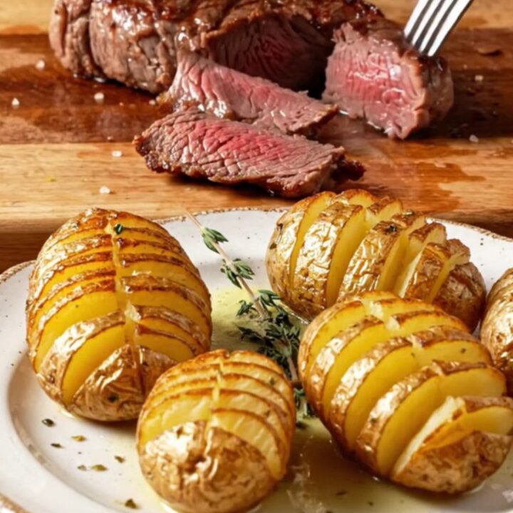 Seared filet mignon sliced and topped with garlic herb butter, beside crispy accordion potatoes