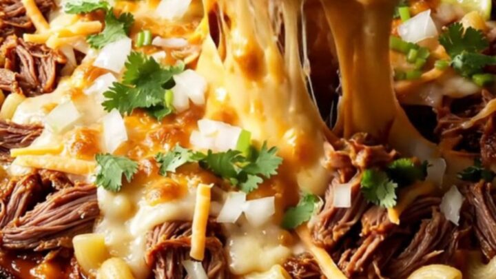 Cast iron skillet filled with bubbling birria mac and cheese, topped with cilantro and lime wedges