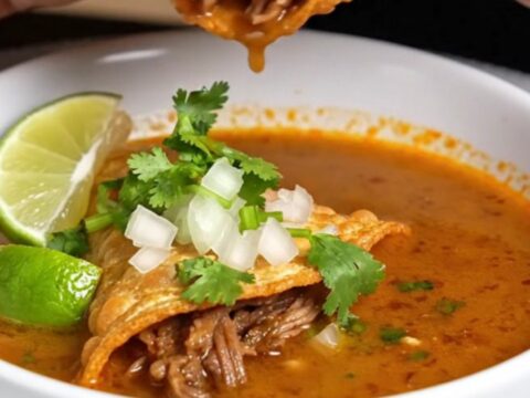 Crispy birria tacos with melted cheese being dipped into a bowl of rich consommé