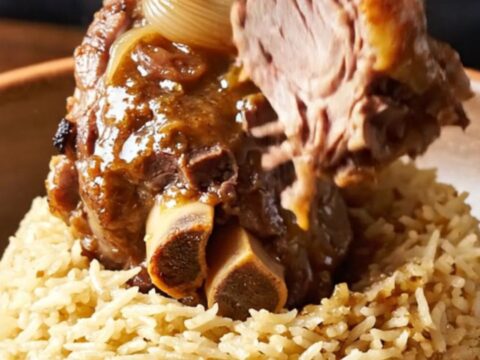 Braised lamb shank on a plate with shallots and glaze, fork pressing tender meat