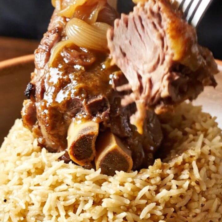 Braised lamb shank on a plate with shallots and glaze, fork pressing tender meat