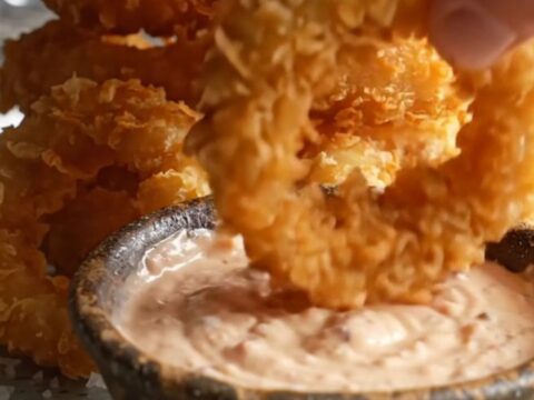 Crispy golden beer-battered onion rings stacked on a platter with a bowl of creamy horseradish dip.