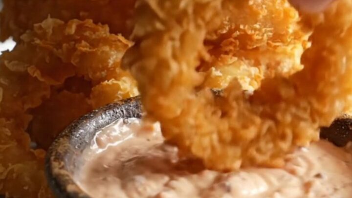 Crispy golden beer-battered onion rings stacked on a platter with a bowl of creamy horseradish dip.