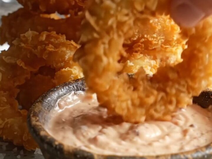 Crispy golden beer-battered onion rings stacked on a platter with a bowl of creamy horseradish dip.