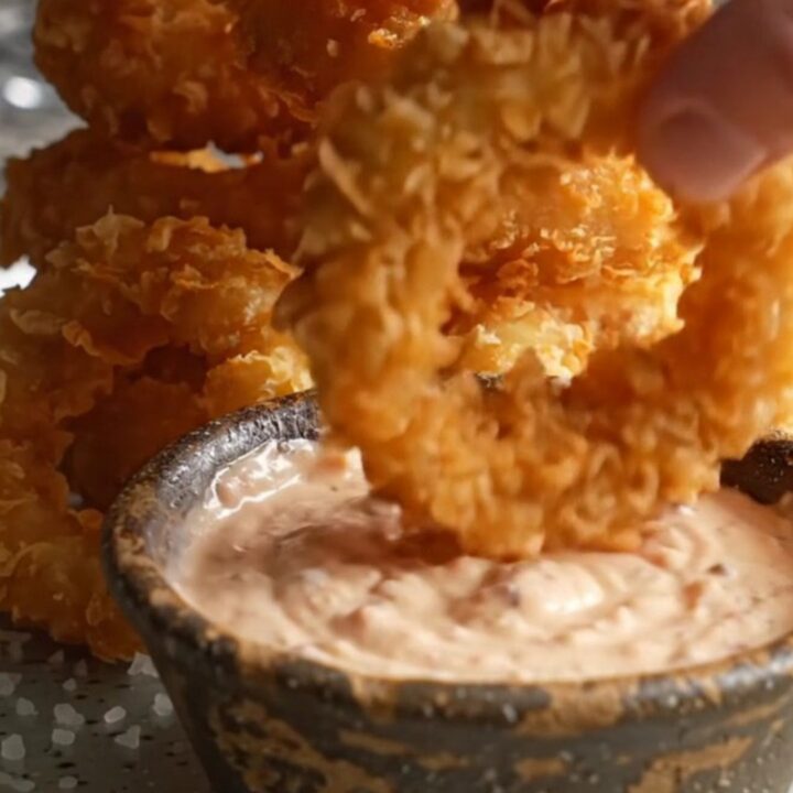Crispy golden beer-battered onion rings stacked on a platter with a bowl of creamy horseradish dip.