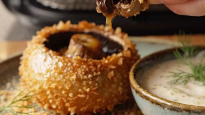 Golden panko-crusted blooming portobello mushroom on a wooden board with garlic herb dip
