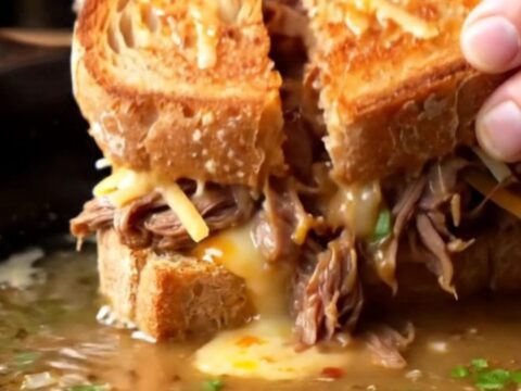Crispy birria grilled cheese sandwich sliced in half, with melted cheese pulling and consommé dip