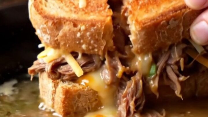 Crispy birria grilled cheese sandwich sliced in half, with melted cheese pulling and consommé dip