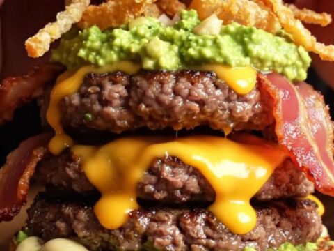Loaded double bacon guacamole burger with crispy onion strings on a wooden board
