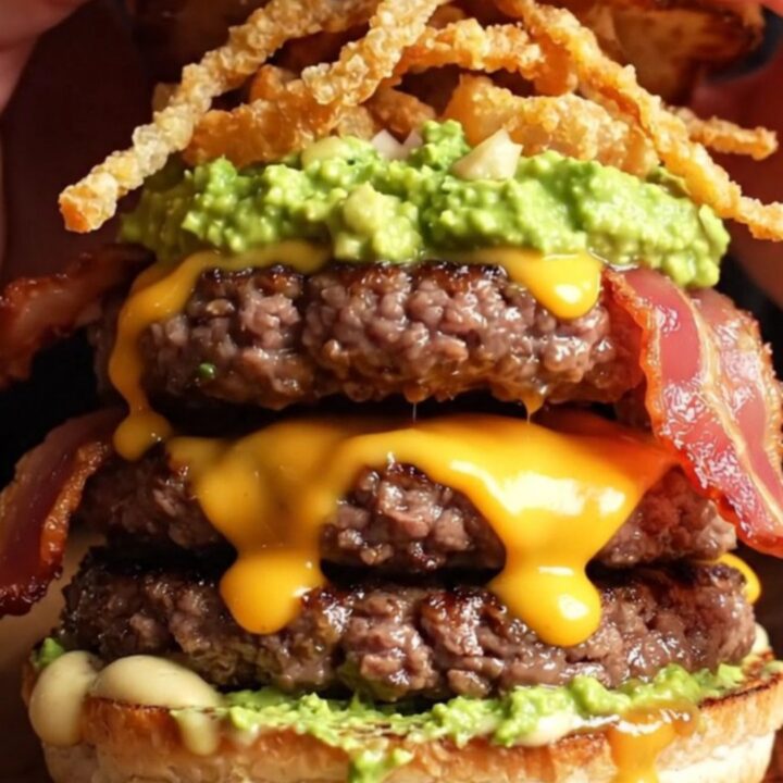 Loaded double bacon guacamole burger with crispy onion strings on a wooden board
