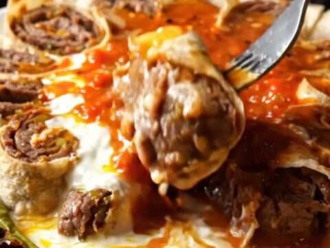 Sliced beyti kebab pinwheels on a platter with garlic yogurt and tomato sauce, drizzled with browned butter.