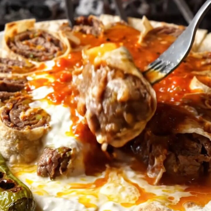 Sliced beyti kebab pinwheels on a platter with garlic yogurt and tomato sauce, drizzled with browned butter.