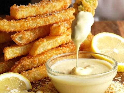 Golden parmesan-crusted asparagus fries piled on a platter with a bowl of lemon aioli