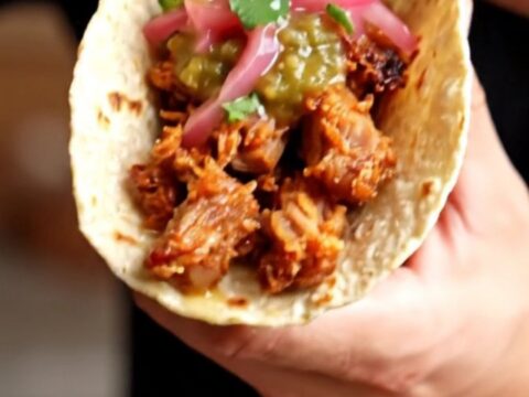 Crispy carnitas tacos topped with salsa verde and pickled red onions on charred corn tortillas