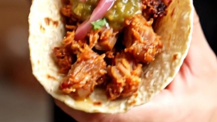 Crispy carnitas tacos topped with salsa verde and pickled red onions on charred corn tortillas