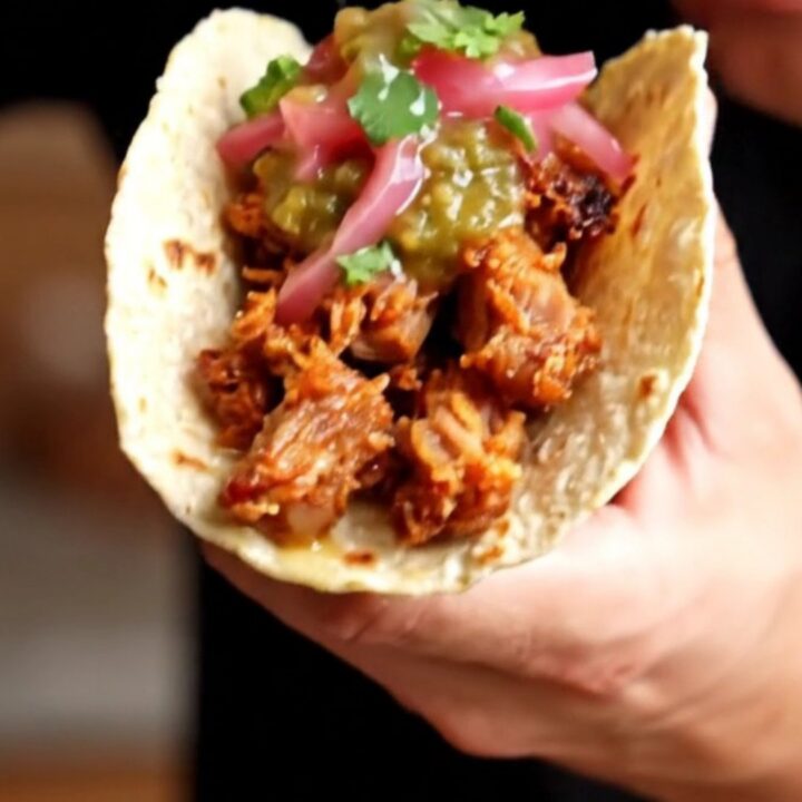 Crispy carnitas tacos topped with salsa verde and pickled red onions on charred corn tortillas