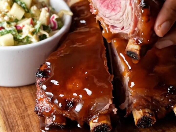Sticky bourbon glazed baby back ribs on a cutting board, sliced between bones, with a glossy caramelized crust.