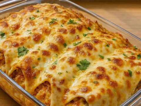 Close-up of a cheesy baked chicken taco being lifted from a glass dish with melted cheese stretching.