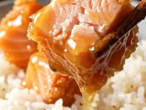 Crispy bang bang salmon bites glazed in a coral sauce, served over coconut rice with green onions and sesame seeds.