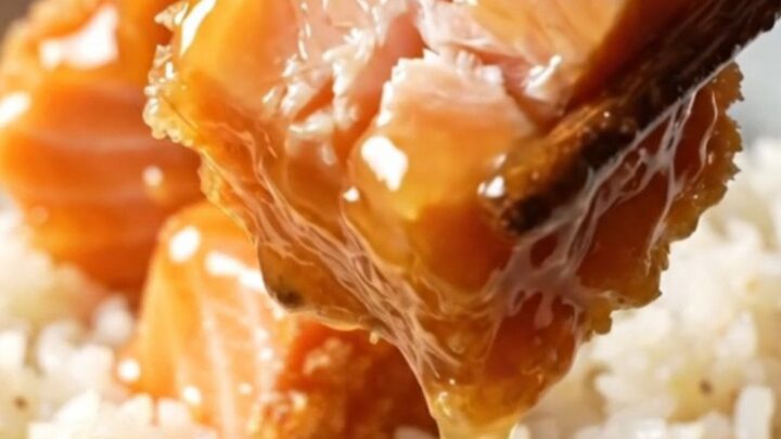 Crispy bang bang salmon bites glazed in a coral sauce, served over coconut rice with green onions and sesame seeds.