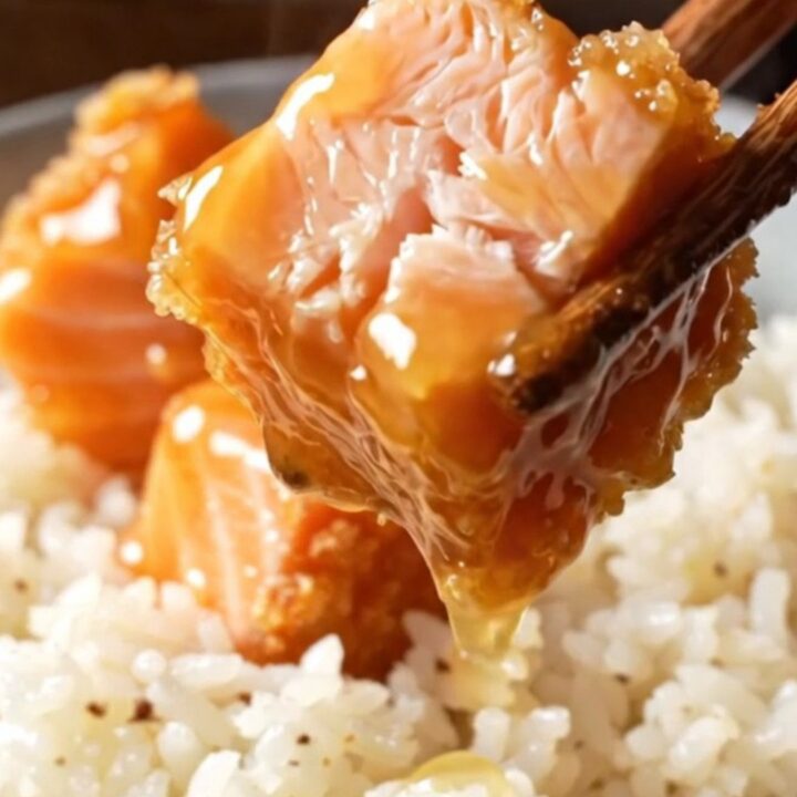 Crispy bang bang salmon bites glazed in a coral sauce, served over coconut rice with green onions and sesame seeds.
