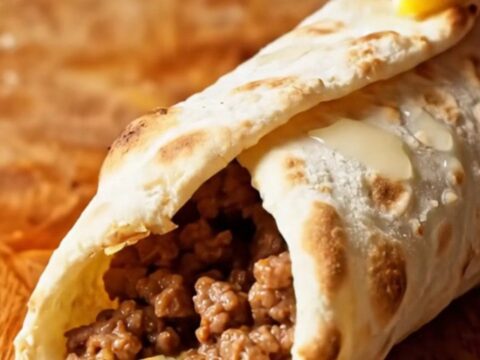 Four rolled lahmacun on a wooden board, garnished with fresh mint and lemon wedges