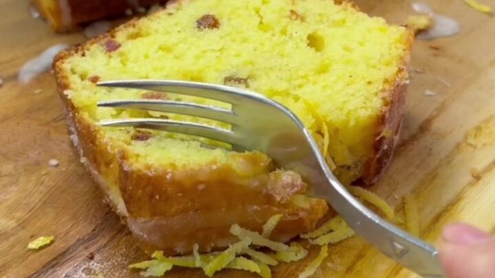 Golden glazed lemon loaf cake with walnuts on a wooden board, sliced to show moist crumb