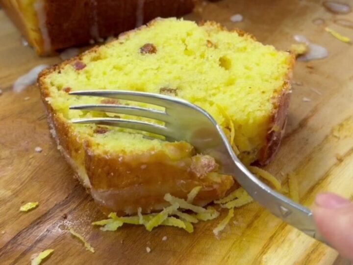 Golden glazed lemon loaf cake with walnuts on a wooden board, sliced to show moist crumb