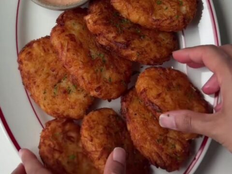 Golden-brown crispy hash brown patties stacked on a plate with a small bowl of tangy dip.