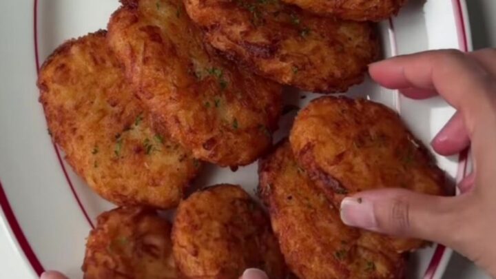 Golden-brown crispy hash brown patties stacked on a plate with a small bowl of tangy dip.
