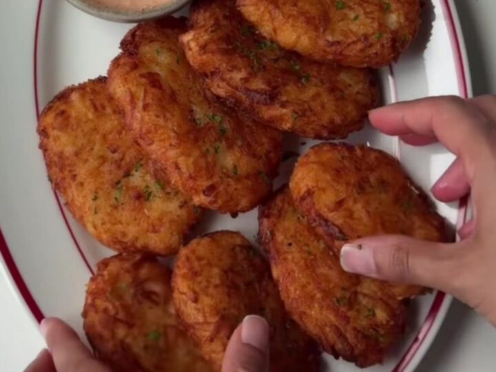 Golden-brown crispy hash brown patties stacked on a plate with a small bowl of tangy dip.