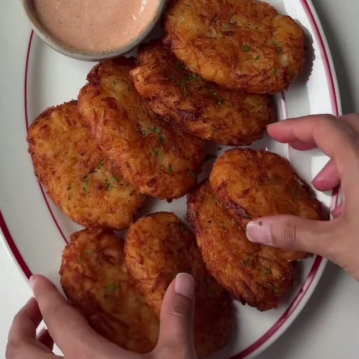Golden-brown crispy hash brown patties stacked on a plate with a small bowl of tangy dip.
