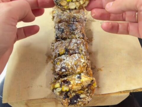 A stack of date and nut bars coated in coconut flakes on a parchment-lined tray.