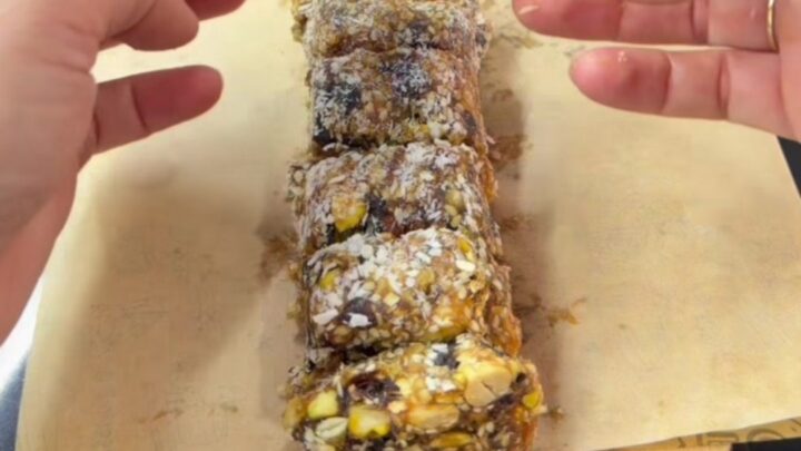 A stack of date and nut bars coated in coconut flakes on a parchment-lined tray.