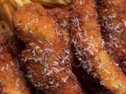 Golden crispy chicken tenders piled on butcher paper with a ramekin of creamy orange dip and fresh parsley