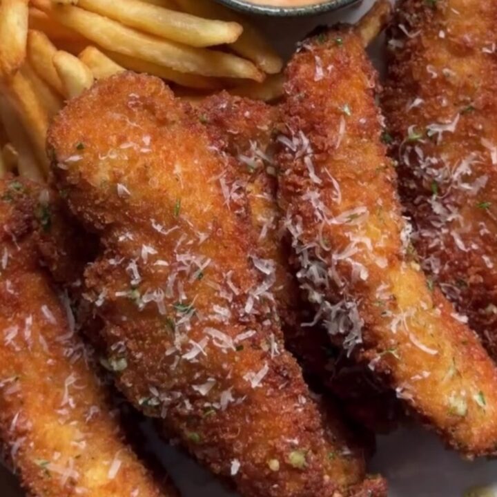 Golden crispy chicken tenders piled on butcher paper with a ramekin of creamy orange dip and fresh parsley