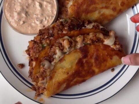 Crispy cheesy tacos topped with lime crema and cilantro on a platter