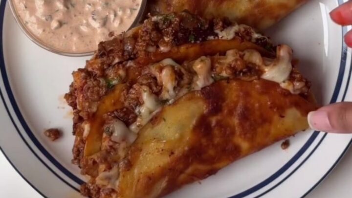 Crispy cheesy tacos topped with lime crema and cilantro on a platter