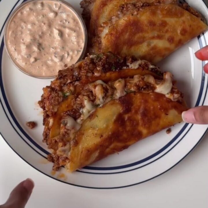 Crispy cheesy tacos topped with lime crema and cilantro on a platter
