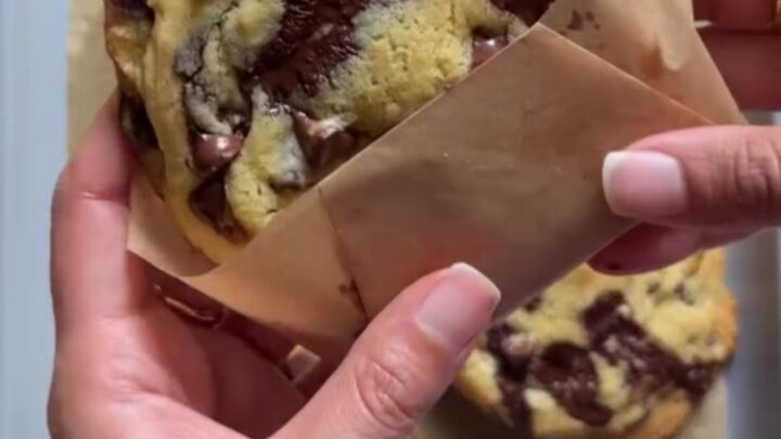 Giant bakery-style two-chip cookies on a wire rack, with melted chocolate and flaky salt