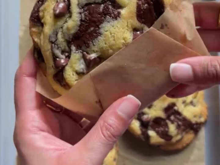 Giant bakery-style two-chip cookies on a wire rack, with melted chocolate and flaky salt