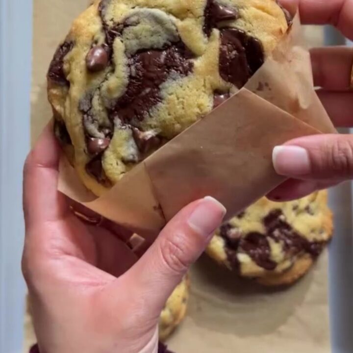 Giant bakery-style two-chip cookies on a wire rack, with melted chocolate and flaky salt