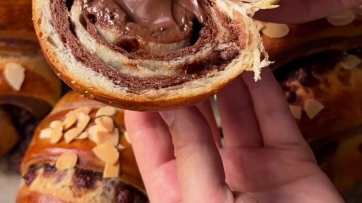 Two-tone chocolate croissant buns on a baking sheet, showing the zebra spiral inside when pulled apart