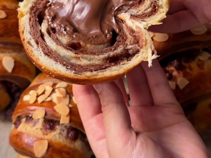 Two-tone chocolate croissant buns on a baking sheet, showing the zebra spiral inside when pulled apart