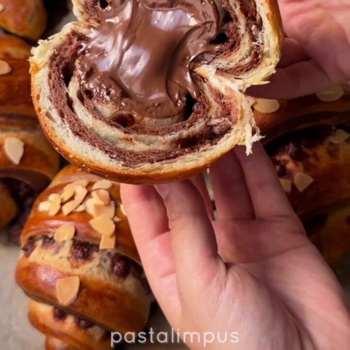 Two-tone chocolate croissant buns on a baking sheet, showing the zebra spiral inside when pulled apart