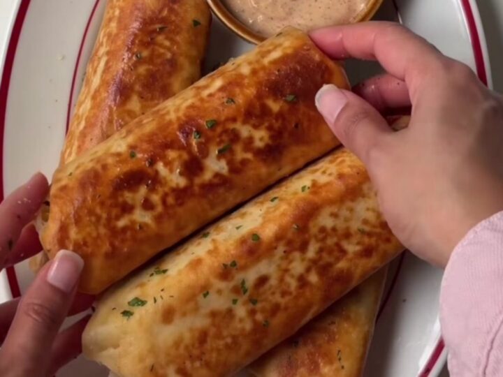 A crispy golden tortilla wrap sliced in half, showing juicy ground beef, melted cheddar, and pickles